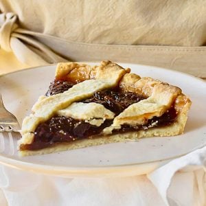 Single slice of lattice fig jam tart on a plate. Beige background.