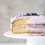 White cake stand with a cut lemon blueberry cake. Gray background.