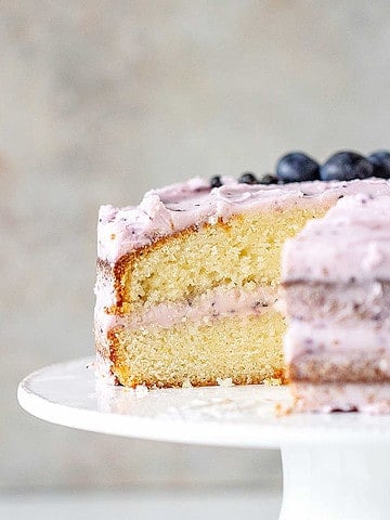 White cake stand with a cut lemon blueberry cake. Gray background.