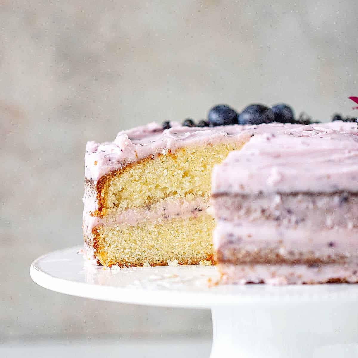 White cake stand with a cut lemon blueberry cake. Gray background.