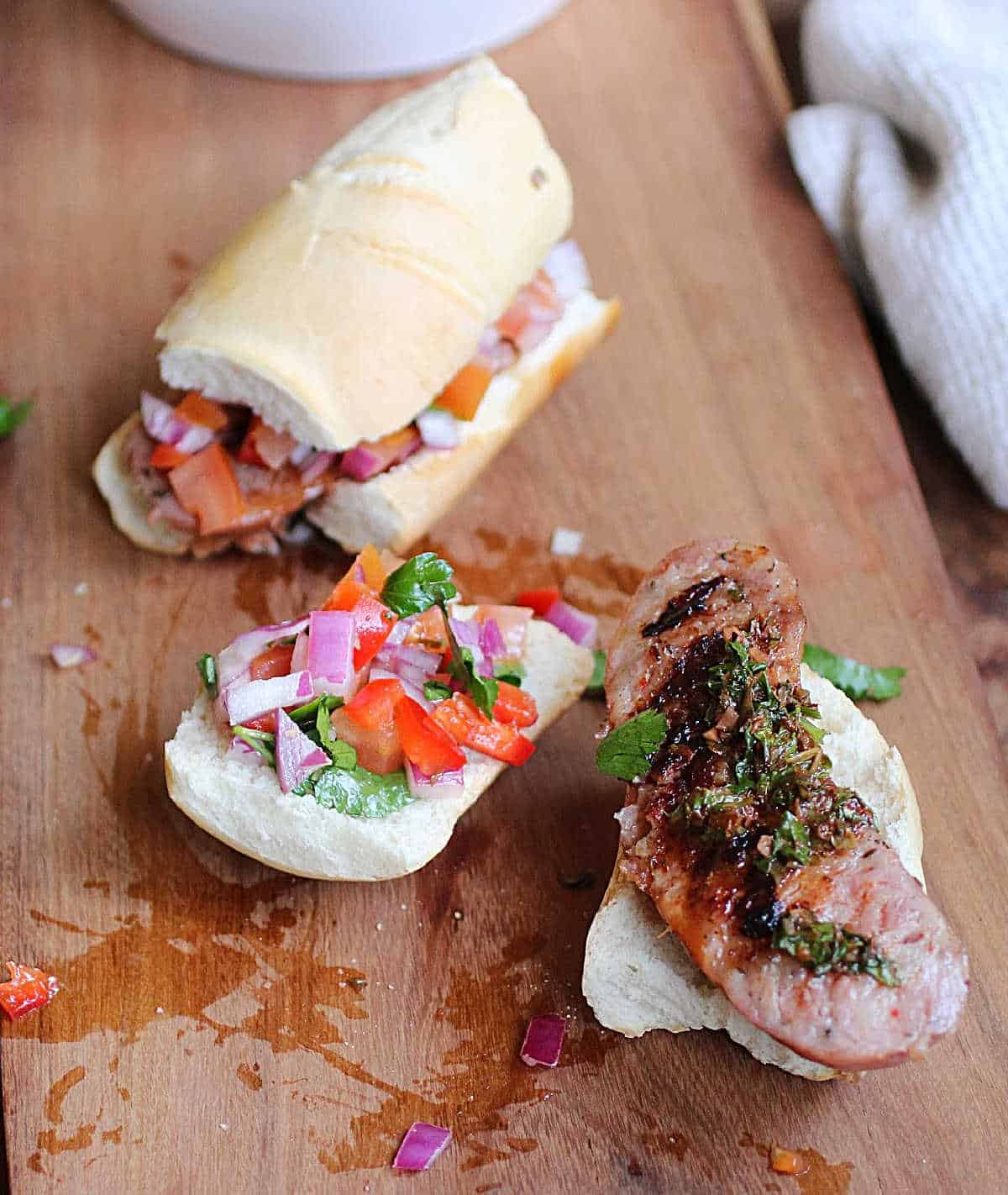 One whole and one open faced choripan sandwiches on a wooden board.