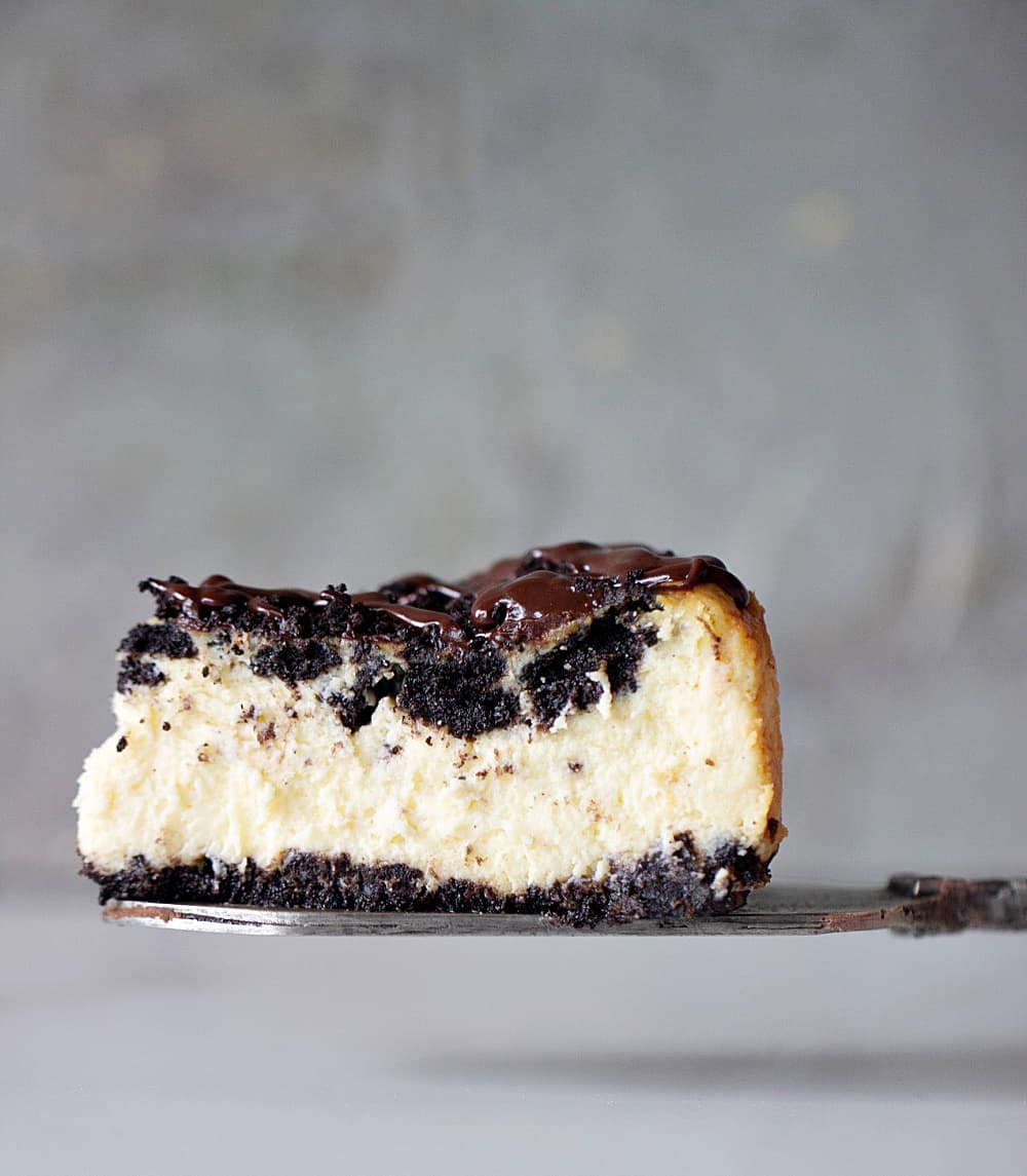 Single slice of Oreo Cheesecake on silver cake server, grey backdrop