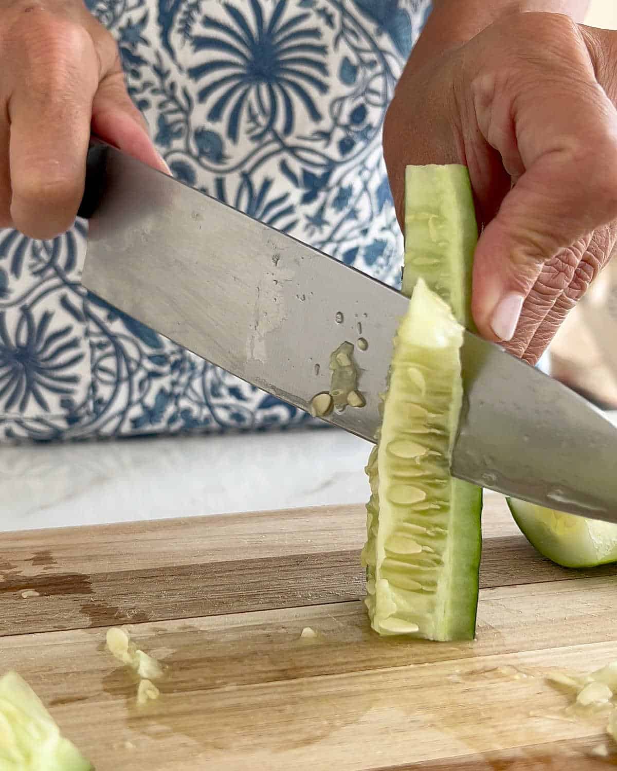 Seeding cucumber quarters with a kitchen knife on a wooden board.