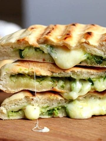 Stack of three filled grilled Naan Breads, oozing cheese on wooden board.