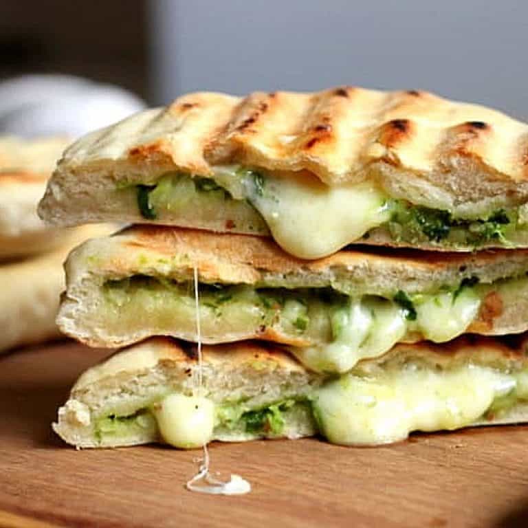 Stack of three filled grilled Naan Breads, oozing cheese on wooden board.