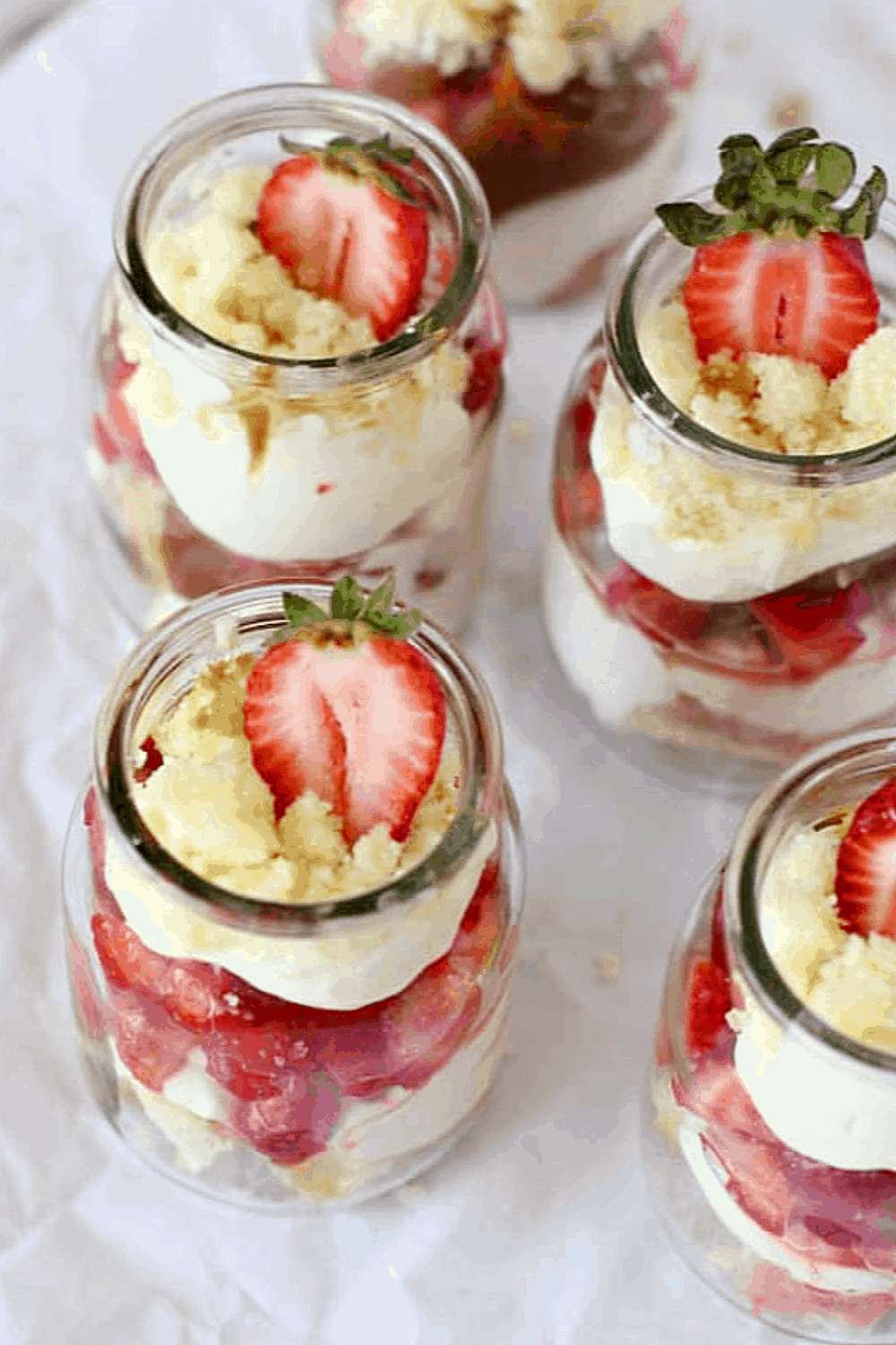 Various glass jars with strawberry trifle, white surface