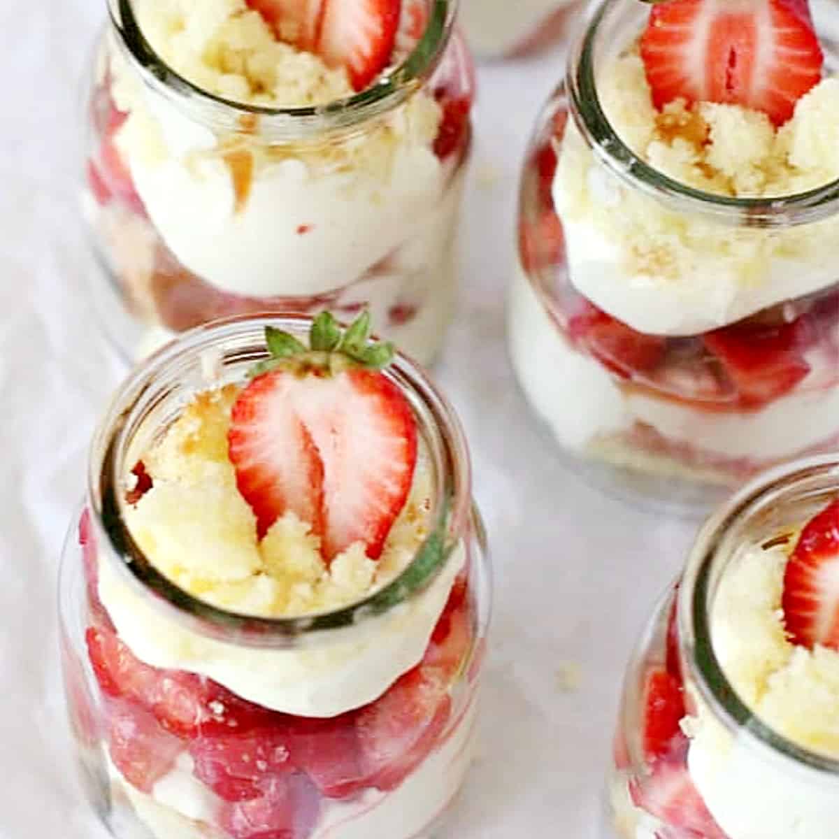 Overview of glass jars with strawberries and cream dessert, white surface