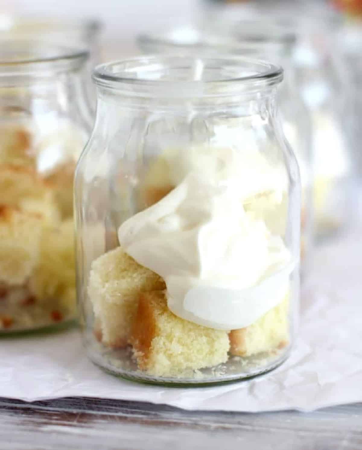 Jars with cake and whipped cream layers. White paper surface. 