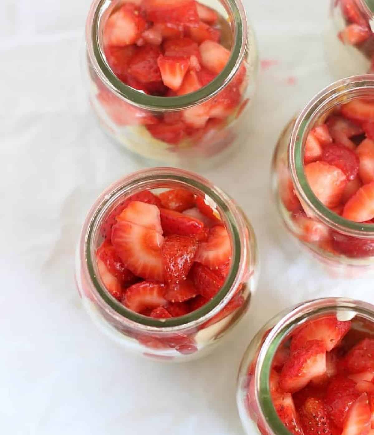 Top view of strawberry layer inside individual trifle jars. White paper surface. 