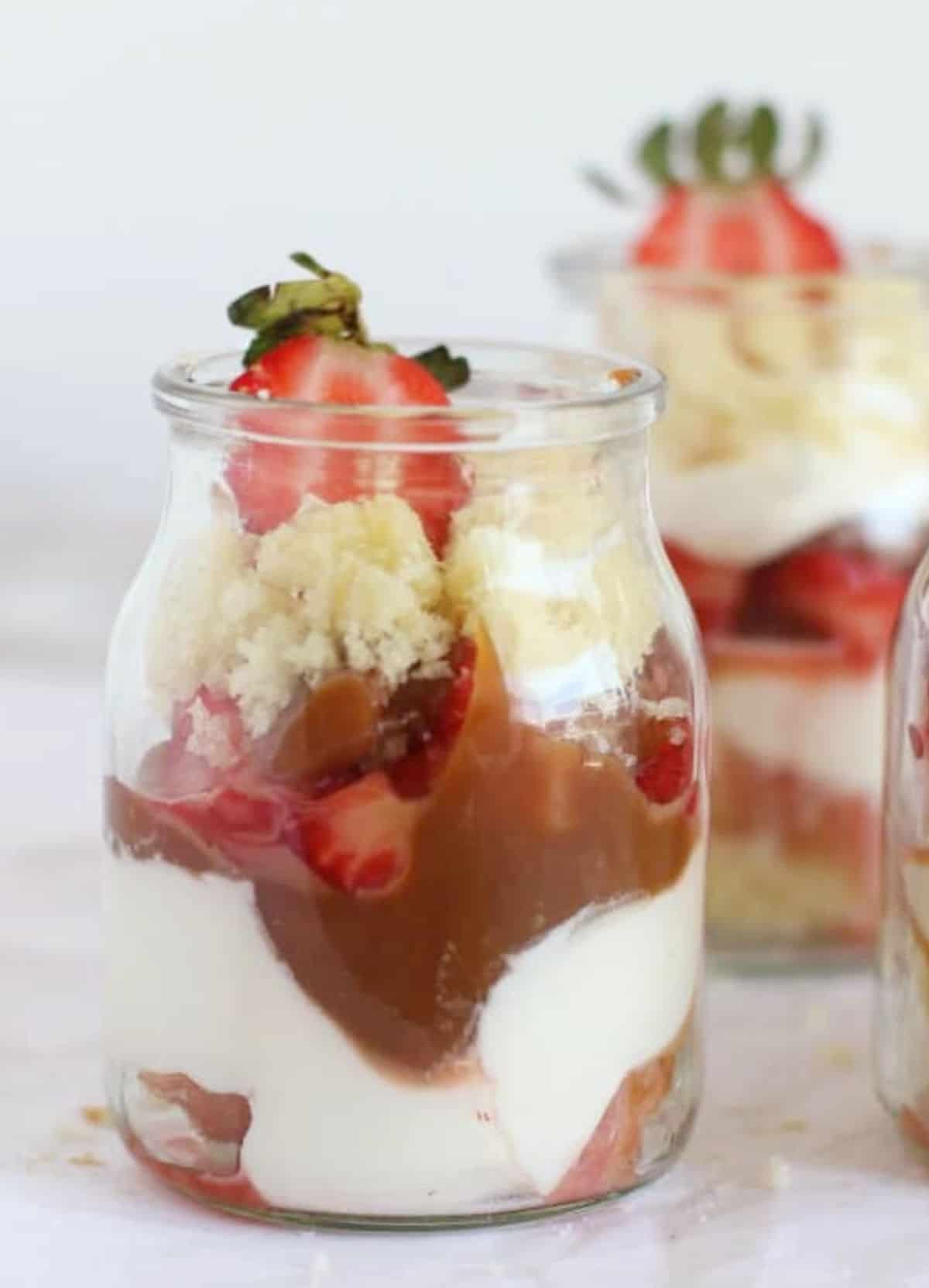Close-up of strawberry dulce de leche trifle in glass jar. White surface and background. 