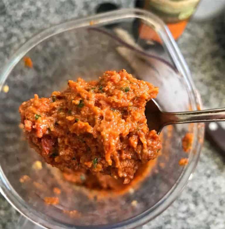 Sun-dried tomato pesto on a spoon, glass jar beneath