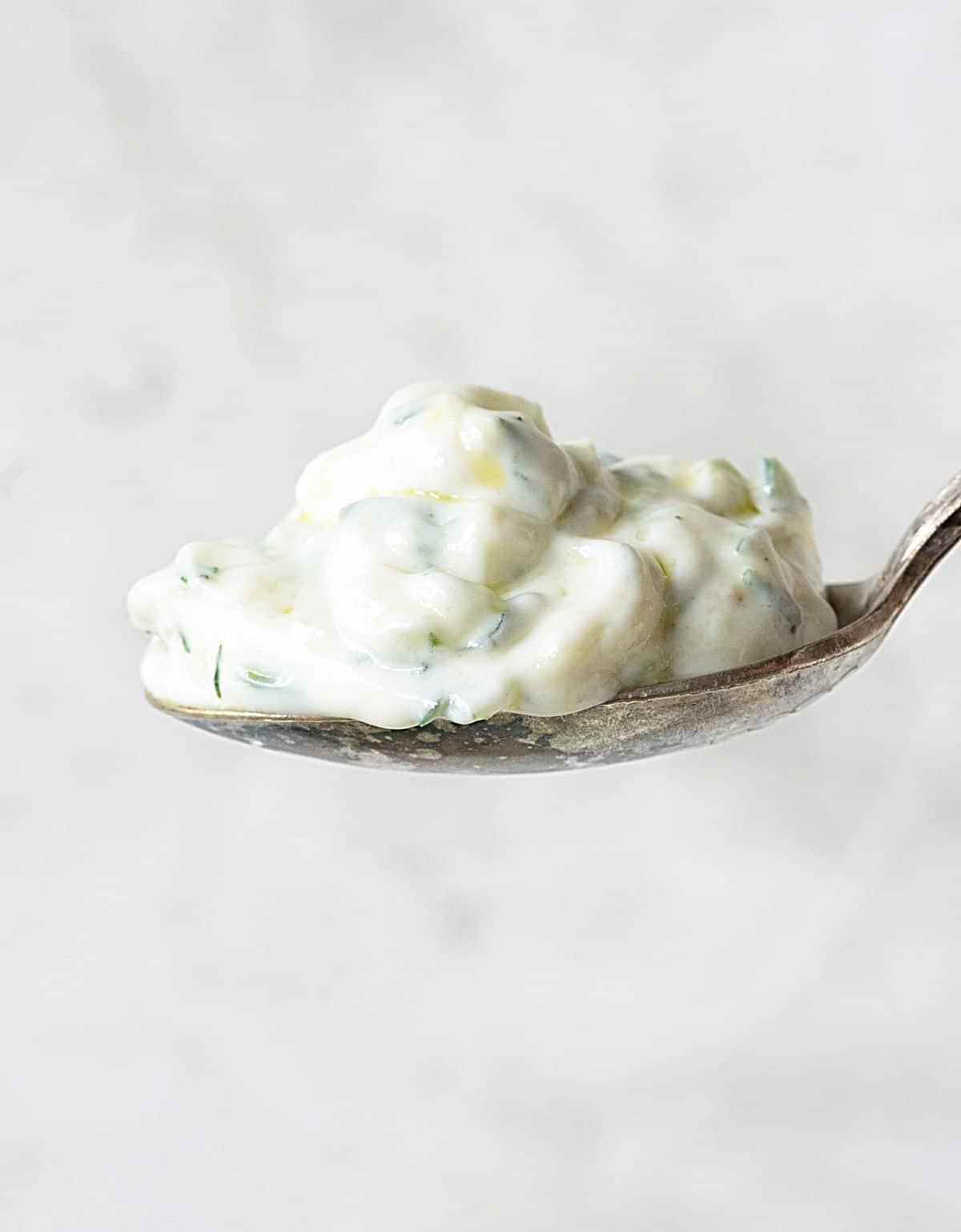 Silver spoon with cucumber yogurt sauce on a grey background. 