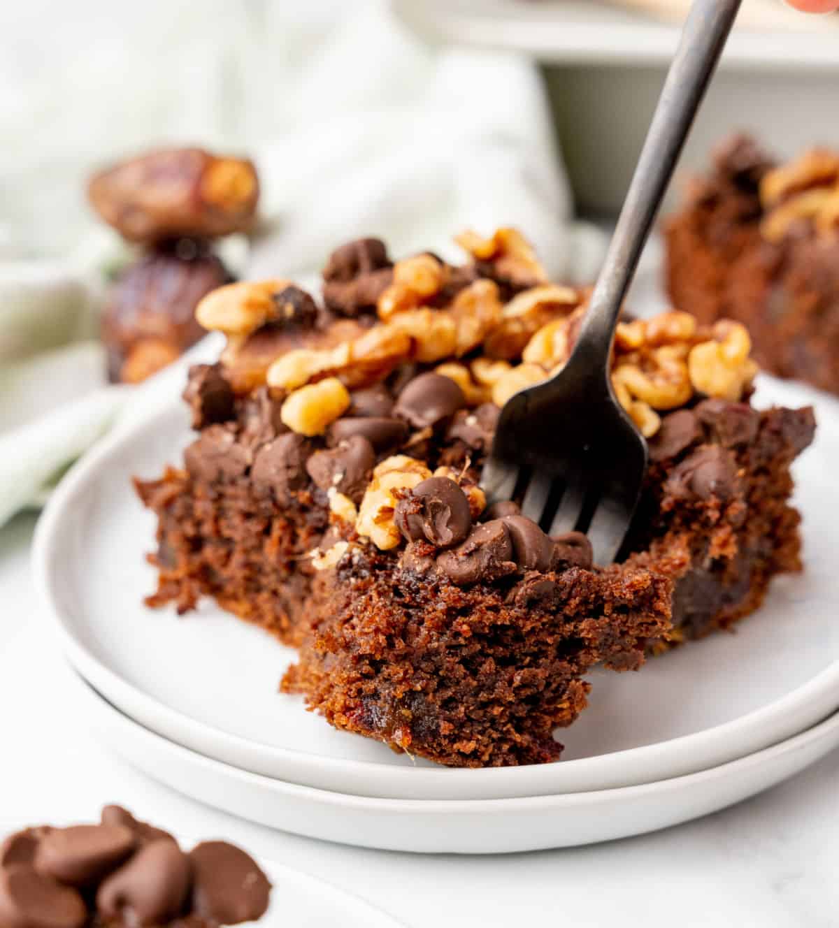 Dark fork with bite of chocolate walnut date cake on a white plate with rest of serving. 