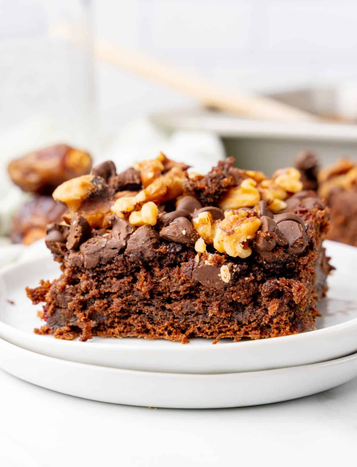 Frontal view of walnut chocolate chip topped date cake on a stack of white plates.