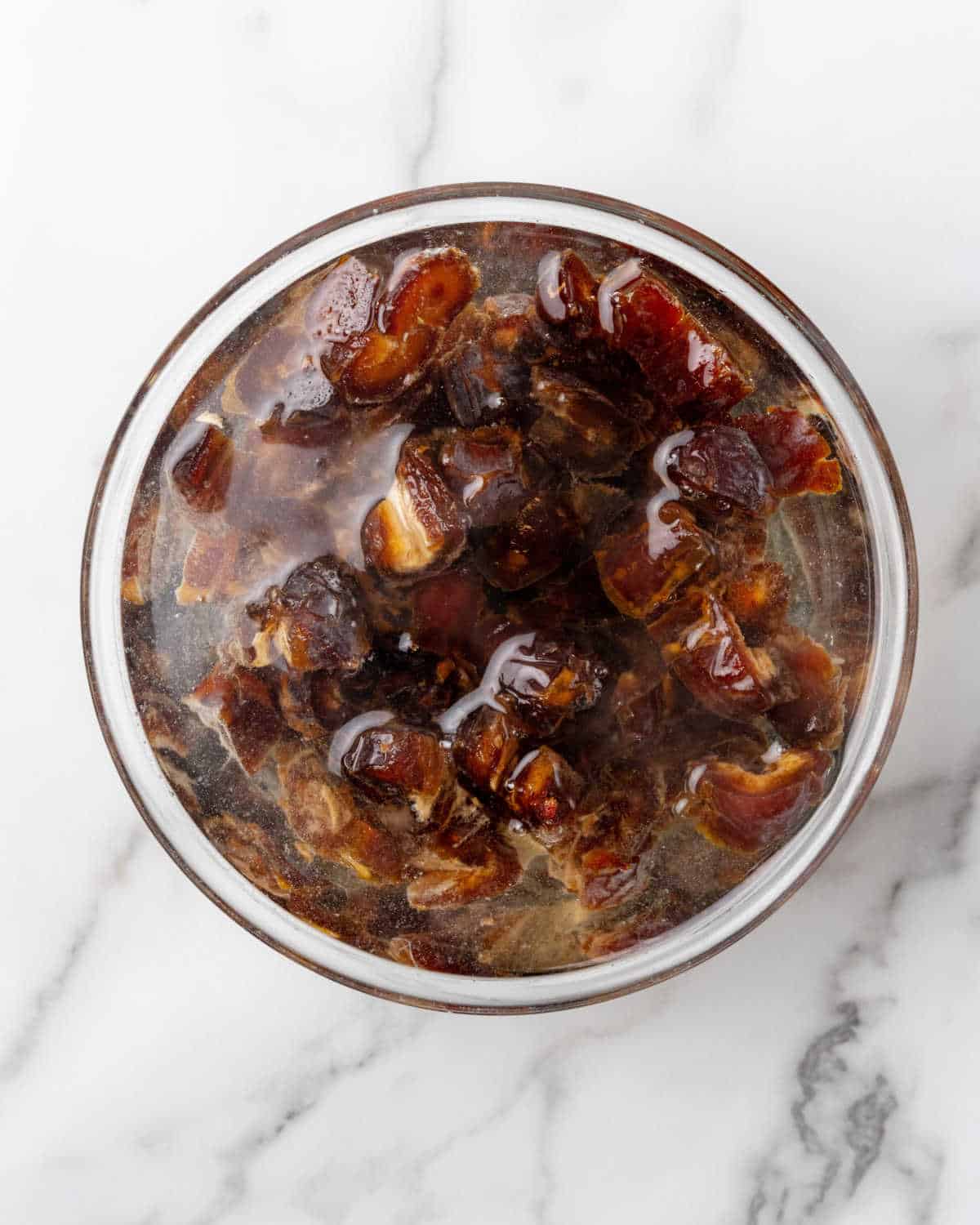 Date covered in water in a glass bowl on a white marble surface. 