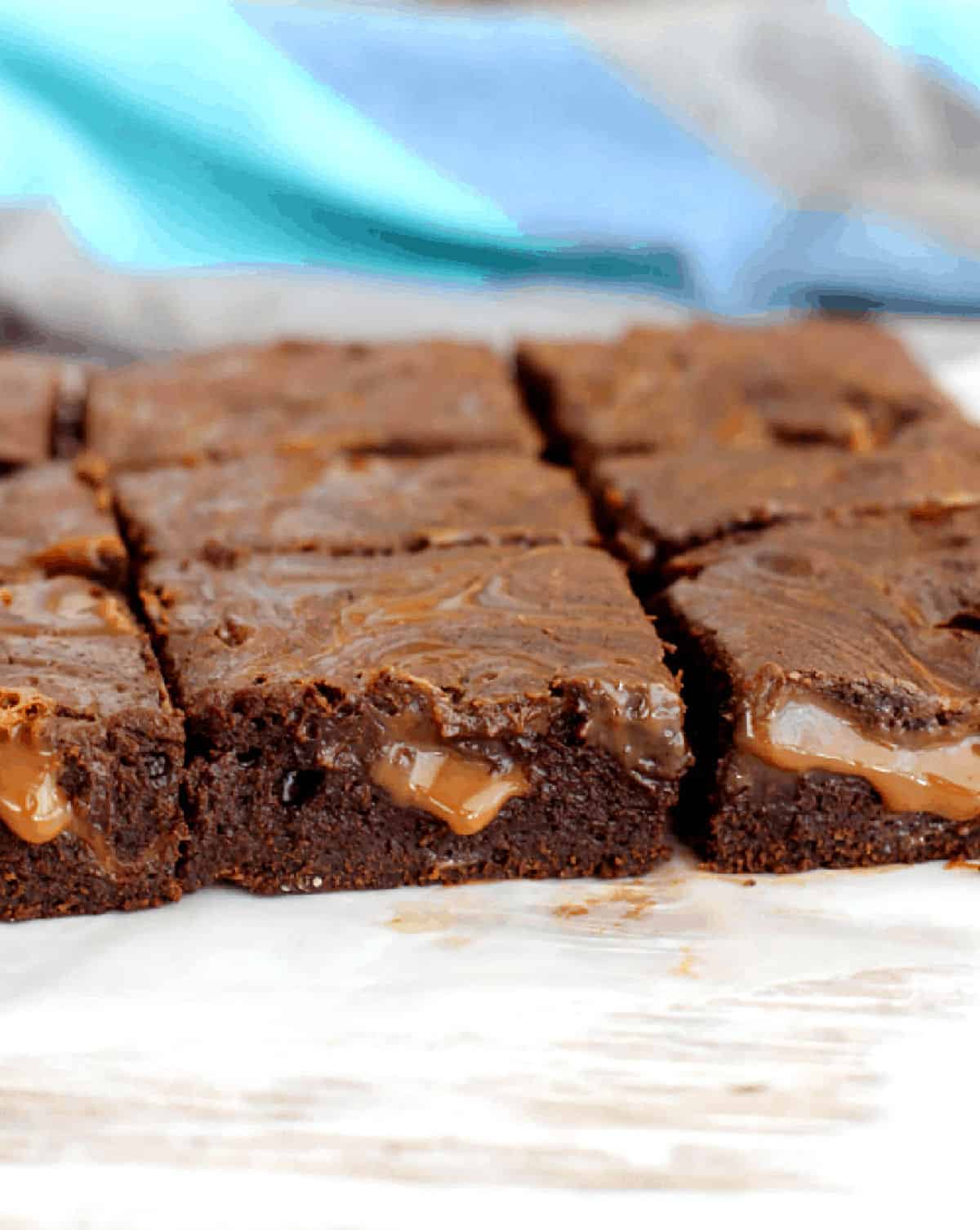 Squares of dulce de leche brownies, white table, blue cloth.