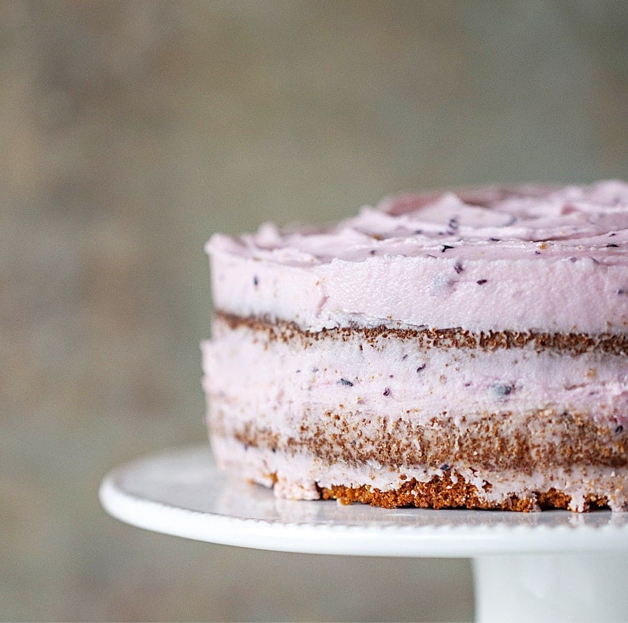 Partial view of frosted lemon blueberry cake on a white cake stand.