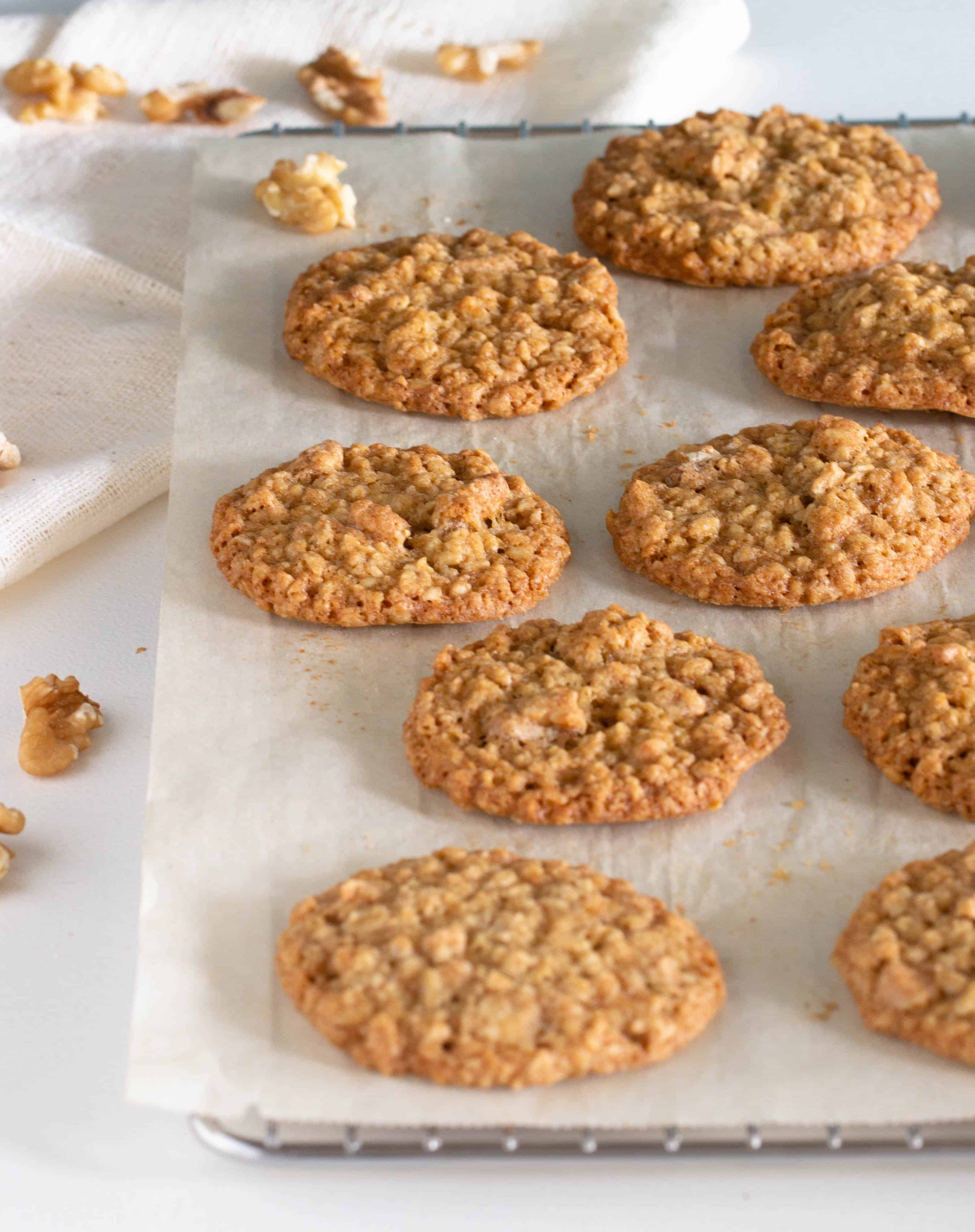 Single layer of oatmeal cookies on parchment paper, white table, loose walnuts