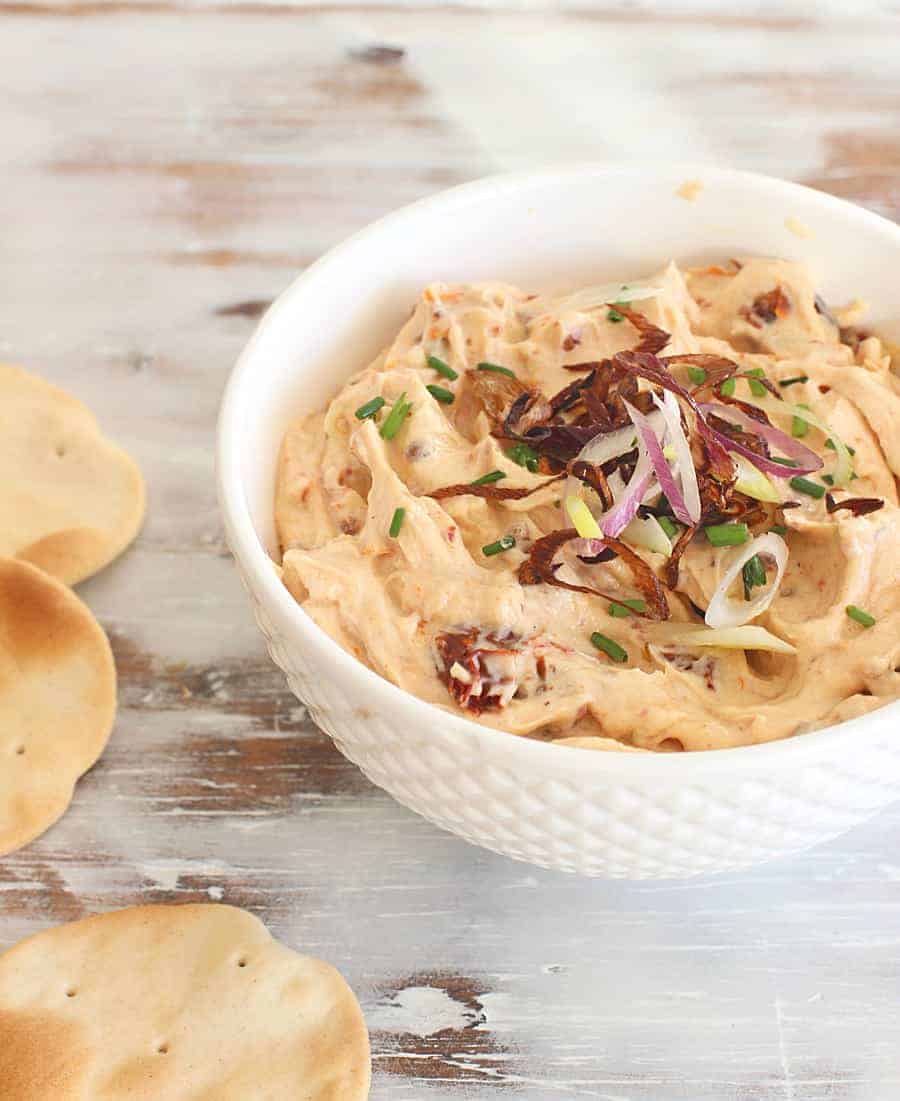 White bowl with tomato dip, crackers on whitish table.