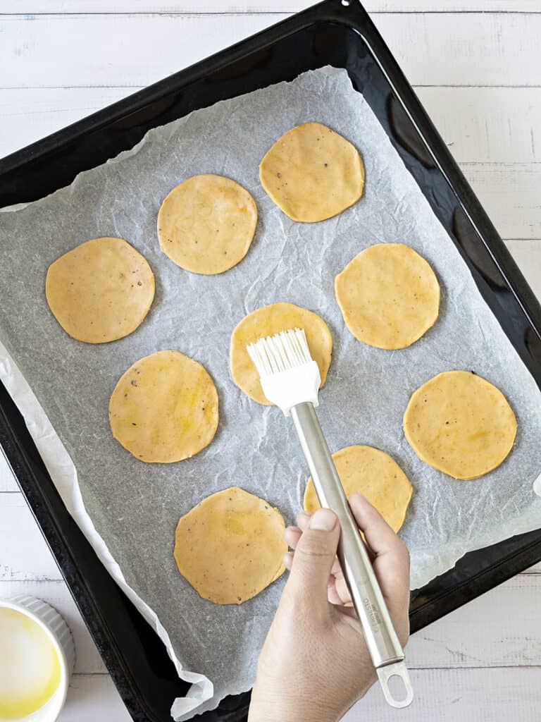 Brushing cracker dough on parchment paper on an oven tray.