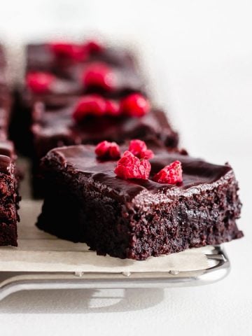 Squares of cocoa brownies, raspberry pieces, wire rack, white surface