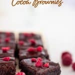 Squares of cocoa brownies, raspberry pieces, white surface, text