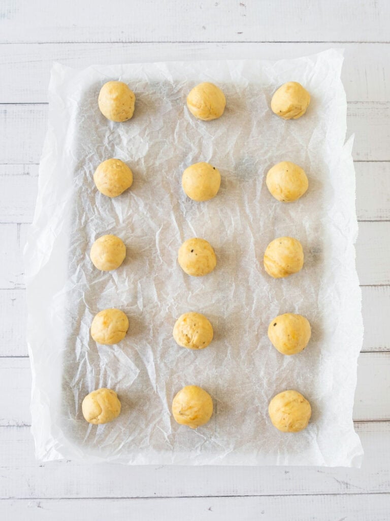 White parchment paper with cracker dough balls on a white surface.