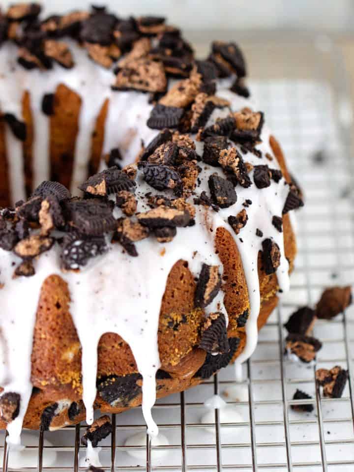 Partial view of glazed bundt cake with chopped oreos on a wire rack