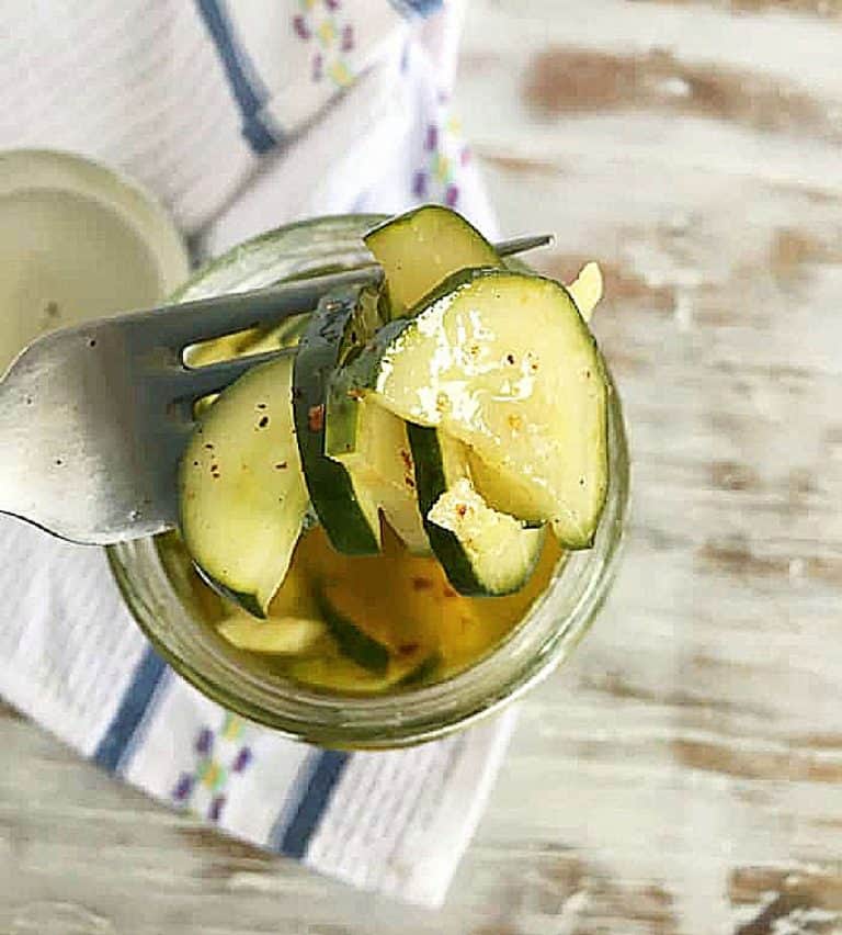 Fork with Pickled Cucumbers, jar underneath, white table, kitchen cloth