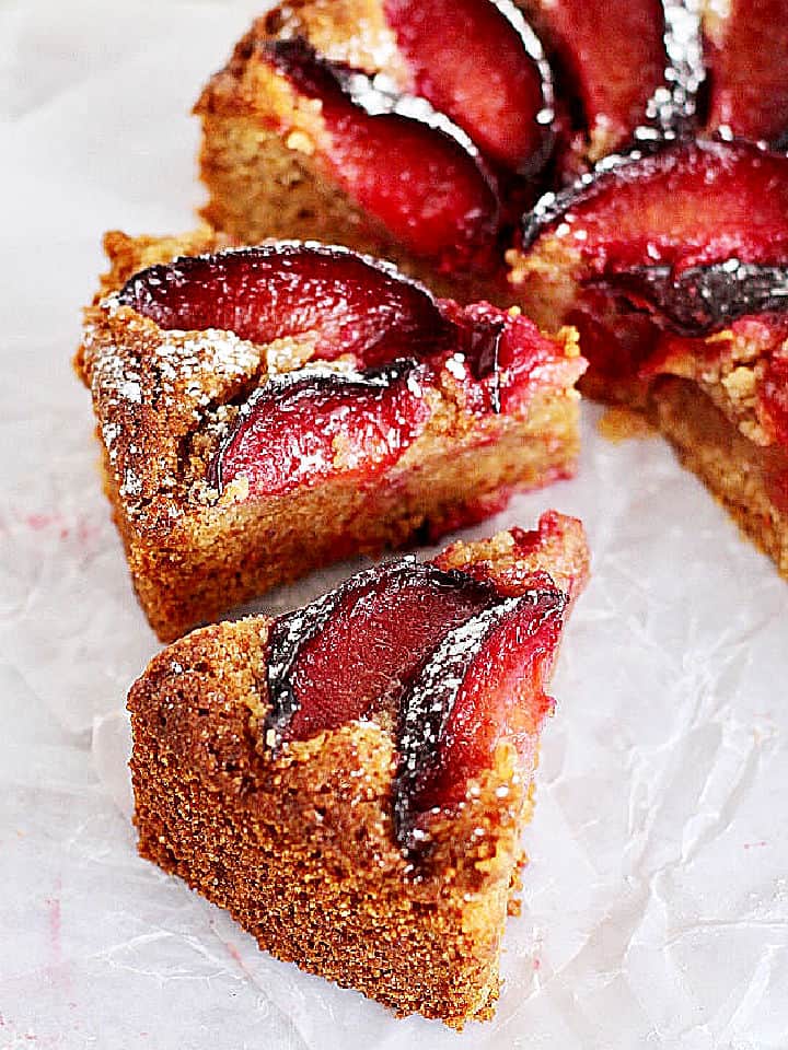 Half cake and slices of plum cake on white parchment paper