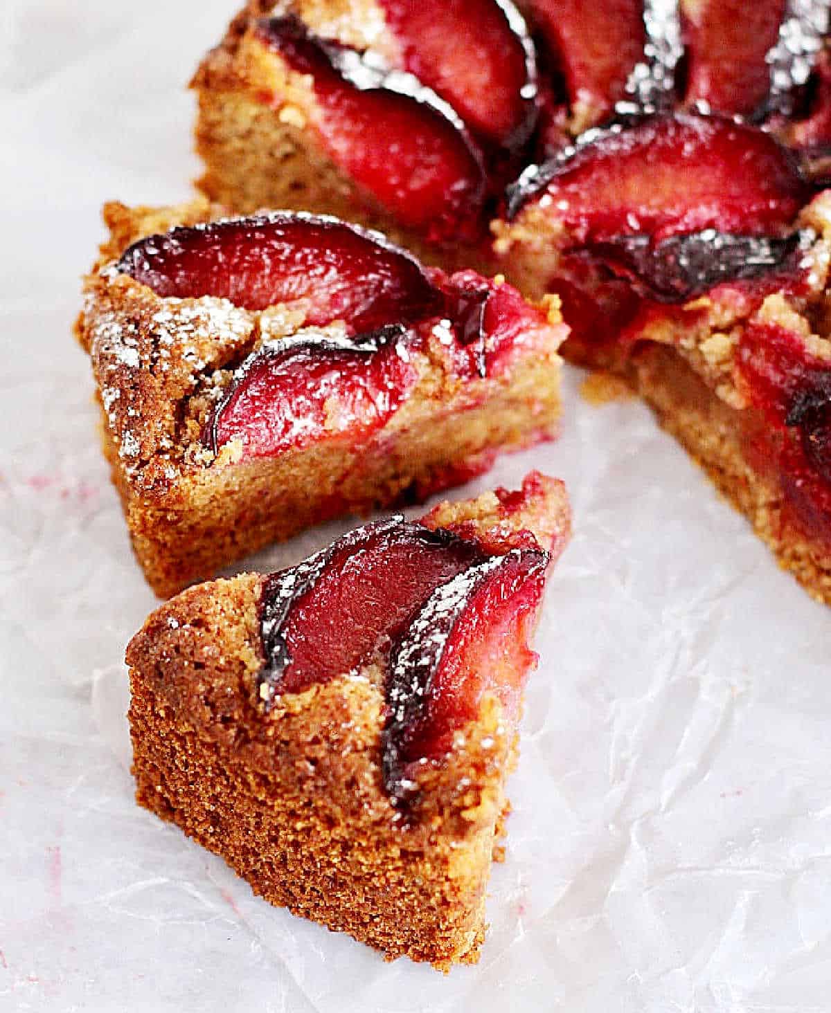 Wedges and half of a honey almond plum cake on a crumpled piece of white paper. 