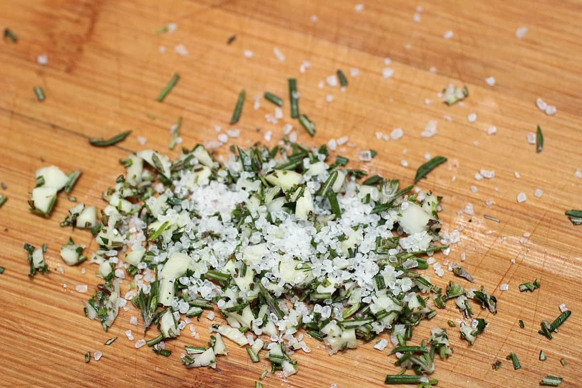 Chopped rosemary and coarse salt on light wooden board