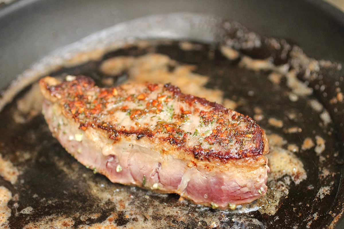 Half cooked steak with butter in dark skillet