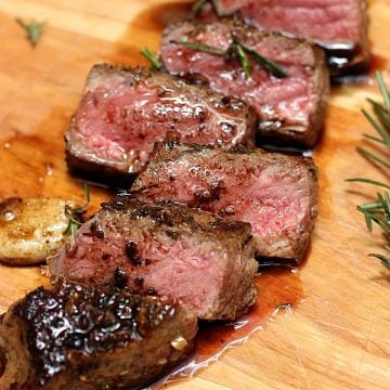 Several cut slices of juicy steak on a wooden board with rosemary.