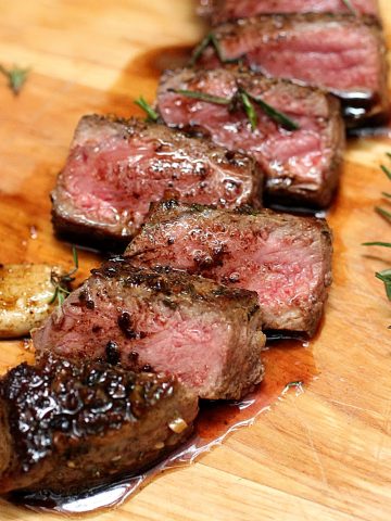 Several cut slices of juicy Rosemary Garlic Butter Steak on wooden board