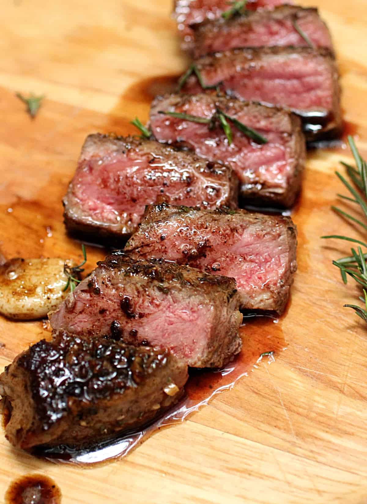 Cut pieces of juicy Rosemary Garlic Butter Steak on wooden board