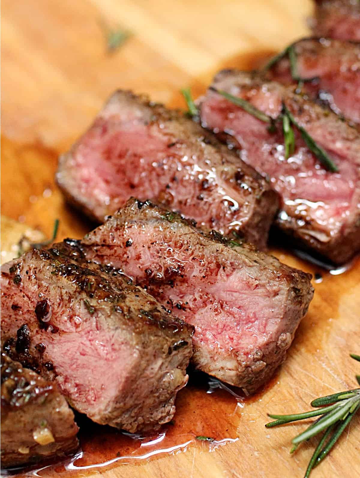 Close up of slices of juicy steak on wooden board, rosemary sprigs