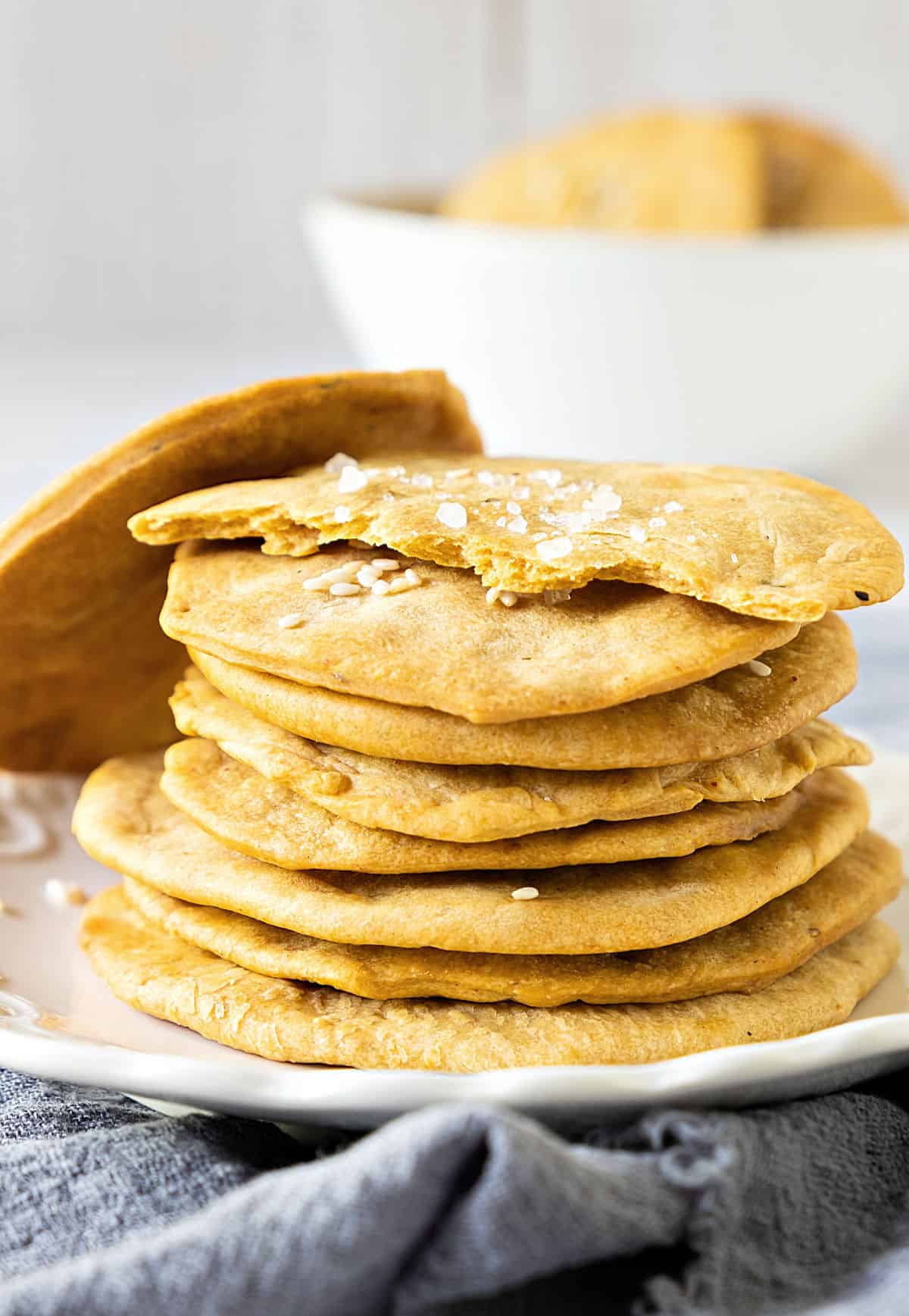 Stack of homemade crackers on a white plate. Blue cloth. Gray background.