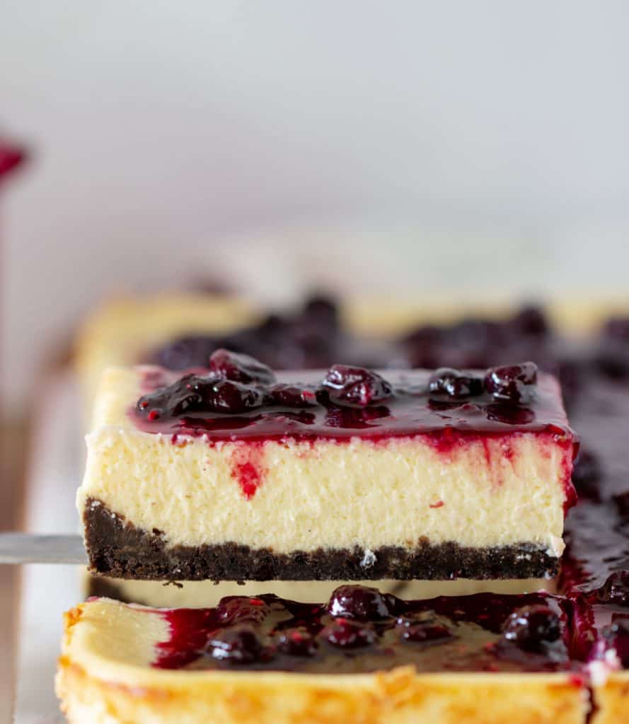 Slice of berry topped cheesecake being lifted from whole cake