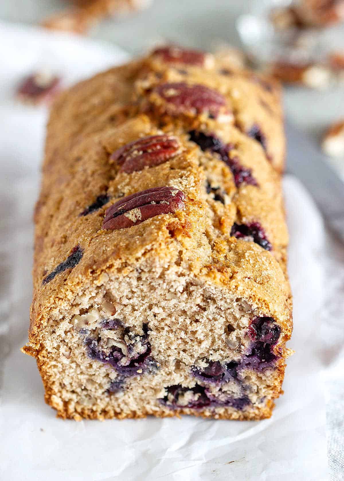 Loaf of blueberry pecan bread on white parchment paper. 