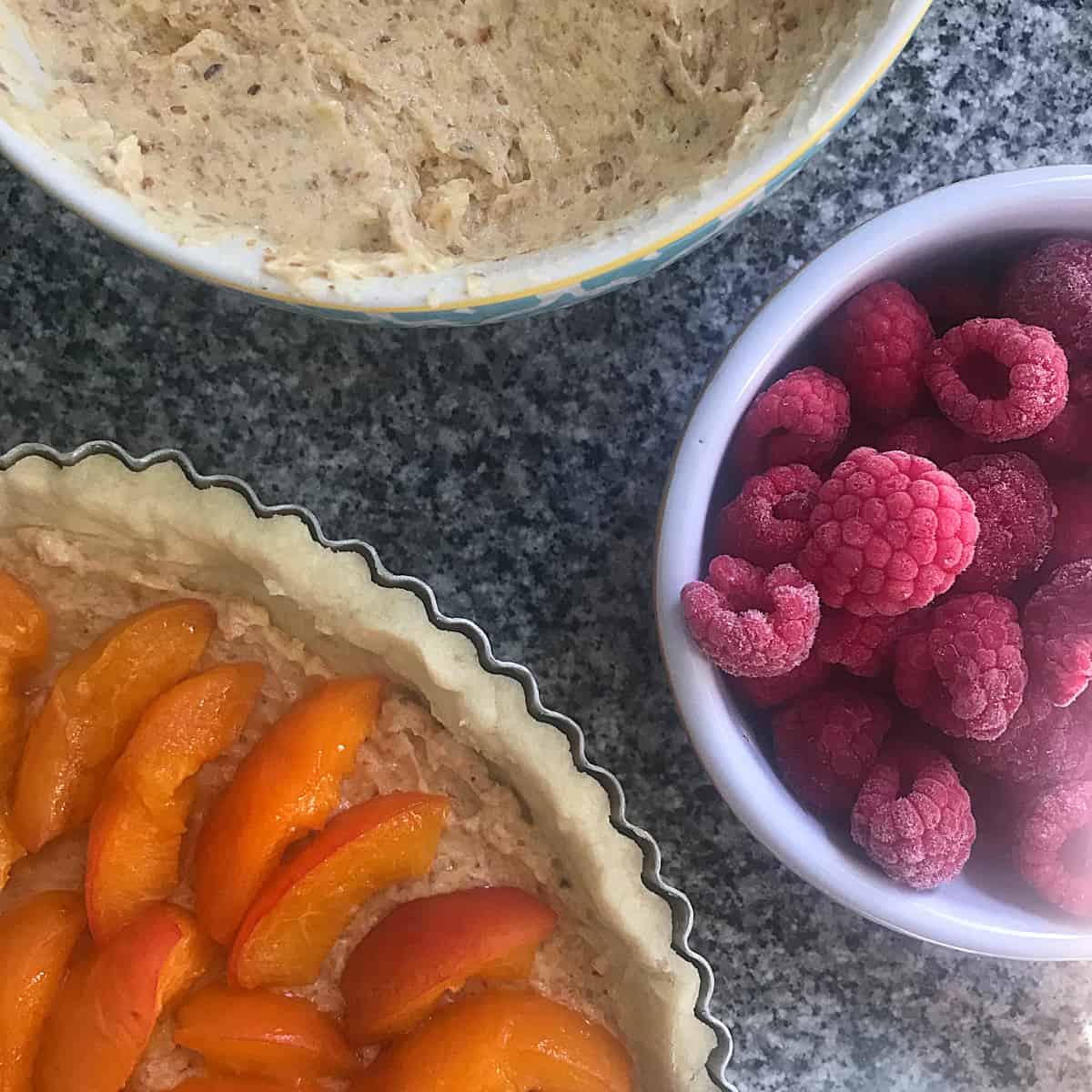 Partial view of crust with apricots, bowl with frangipane, raspberries in bowl