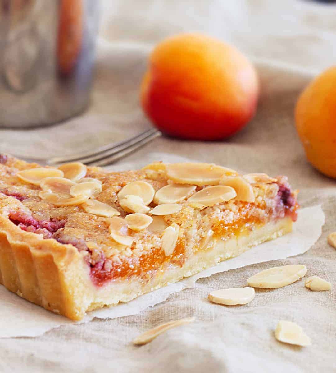 Slice of apricot tart on beige cloth, whole apricots, loose almonds
