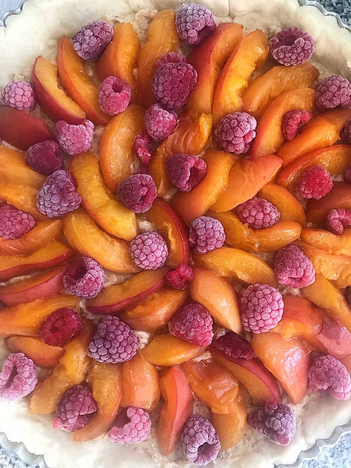 Close up of unbaked pie crust filled with apricots and raspberries.