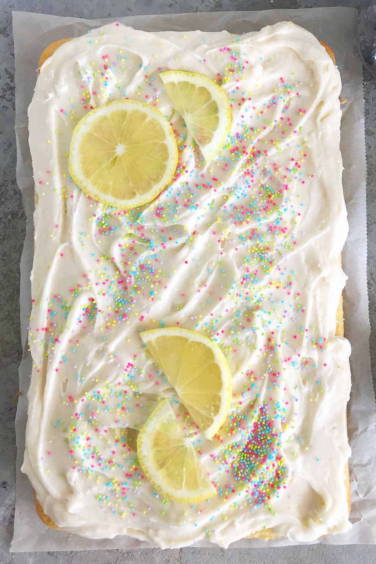 Top view of frosted lemon sheet cake with sprinkles and lemon slices.