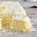 Frosted squares of lemon coconut cake on a grey surface.
