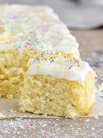 Frosted squares of lemon coconut cake on a grey surface.