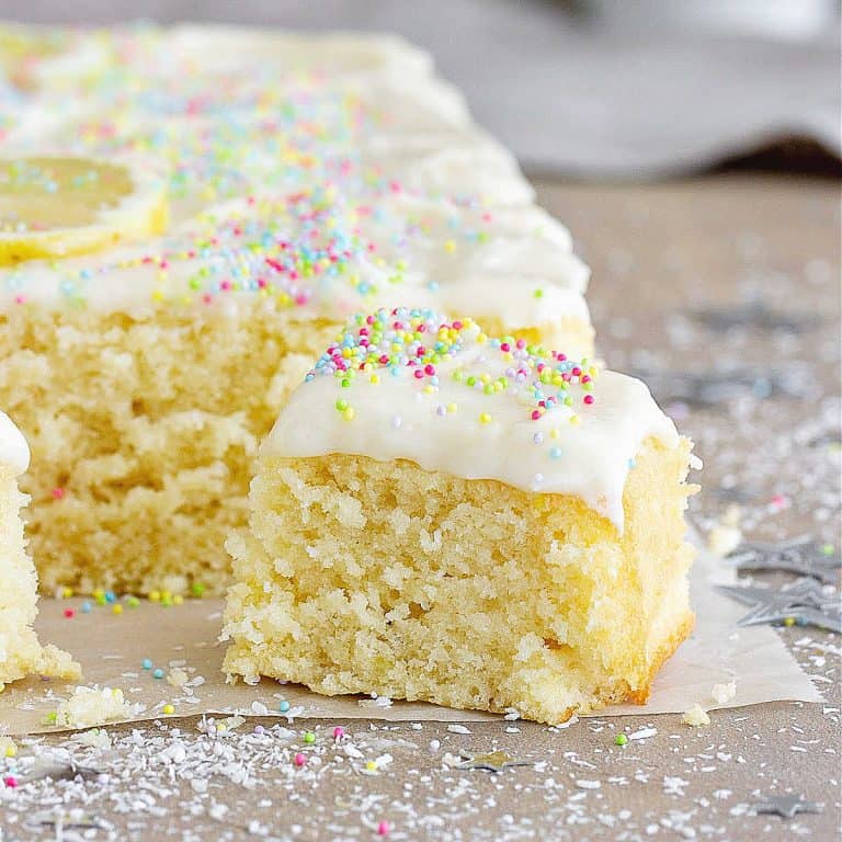 Frosted squares of lemon coconut cake on a grey surface.