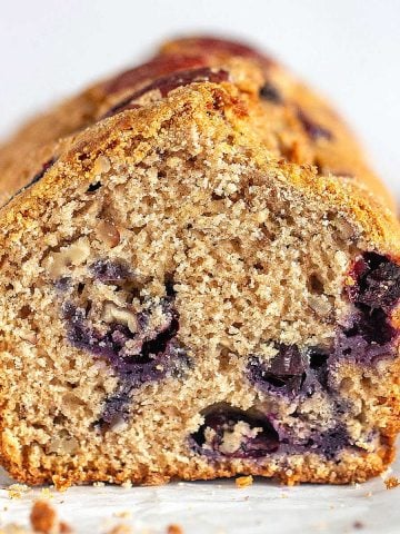 Cut loaf of blueberry bread on a white surface and white background.