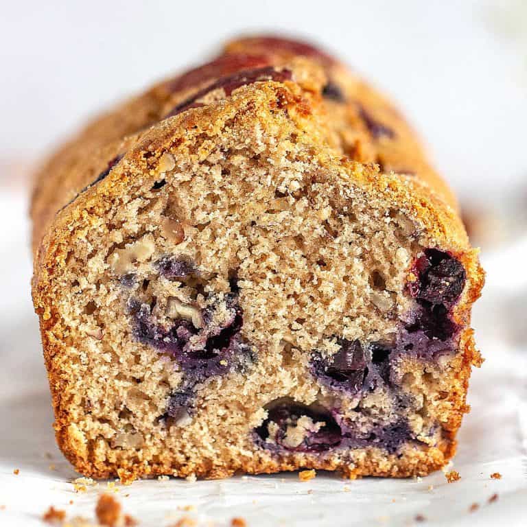 Cut loaf of blueberry bread on a white surface and white background.