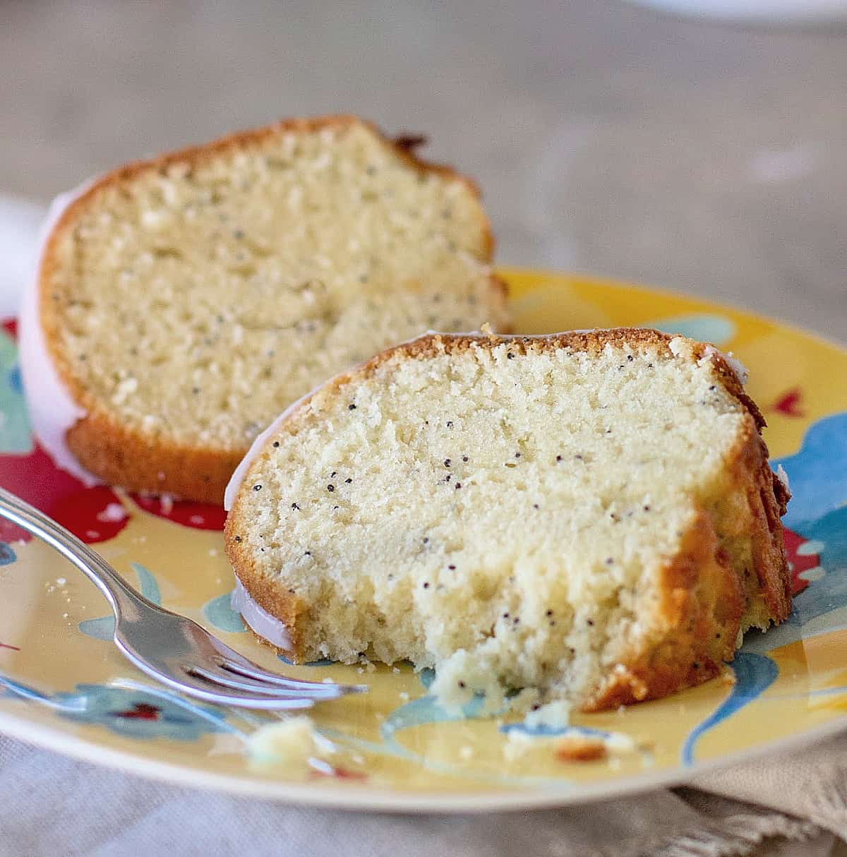 Close-up of slices of poppy seed bundt cake on a colorful plate, a silver fork, grey surface